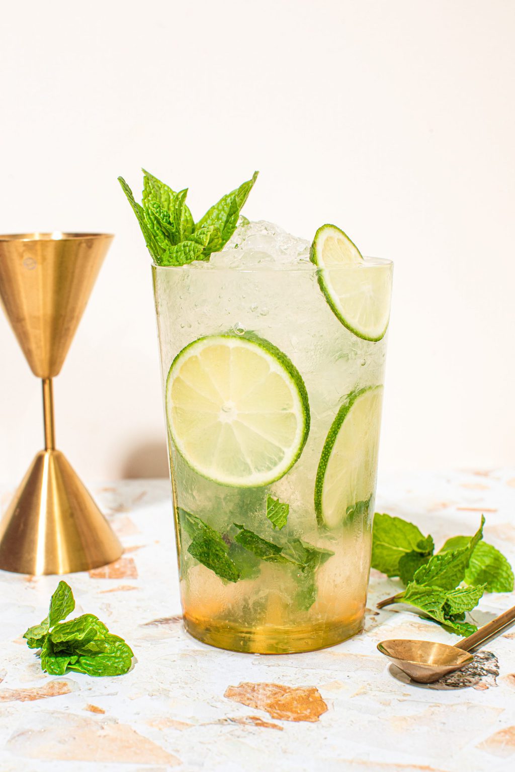 mocktail mojito in highball glass with lime wheels, mint sprig and jigger on side