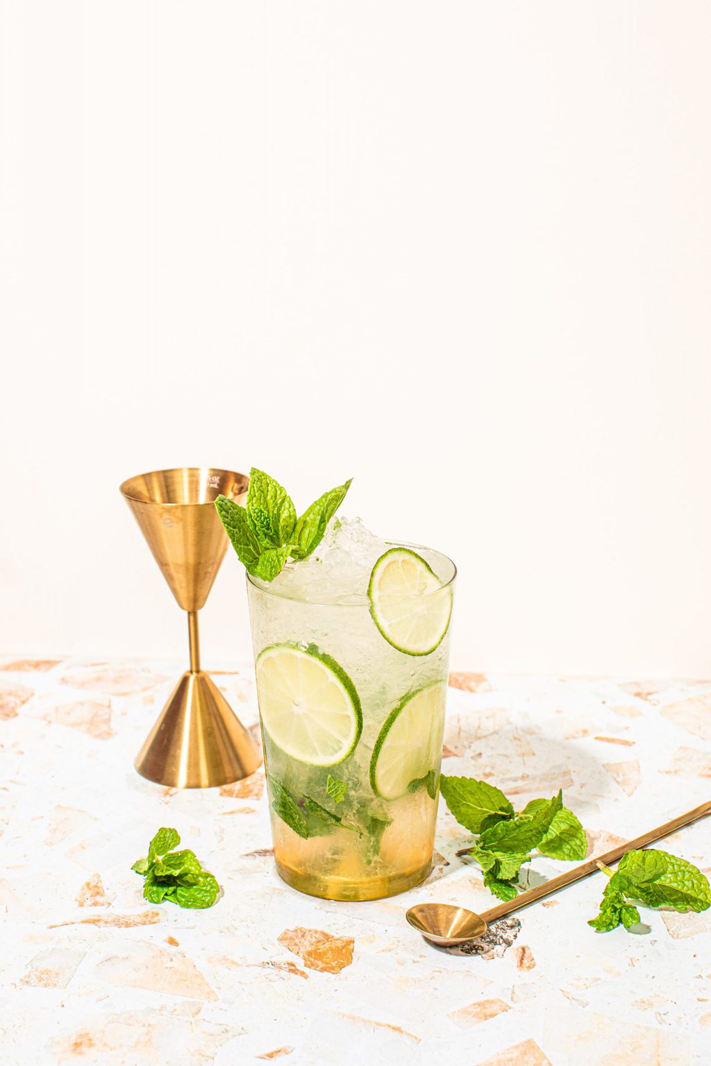 mocktail mojito in highball glass with lime wheels, mint sprig and jigger on side