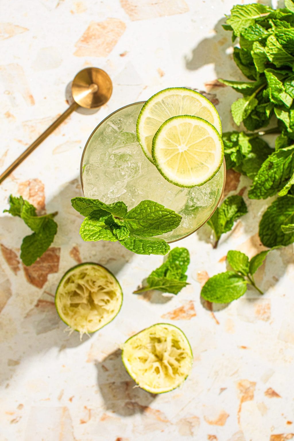 overhead of mint mojito mocktail with mint sprigs, bar spoon and squeezed lime