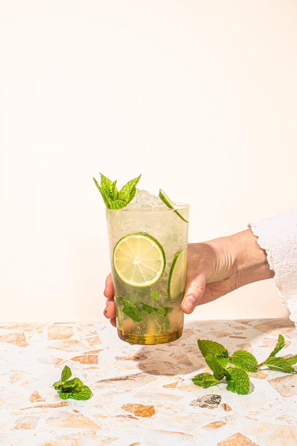 hand holding highball glass filled with virgin mint mocktail with lime wheels and fresh mint