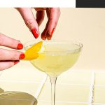 two hands placing lemon peel on lemon martini in coupe glass