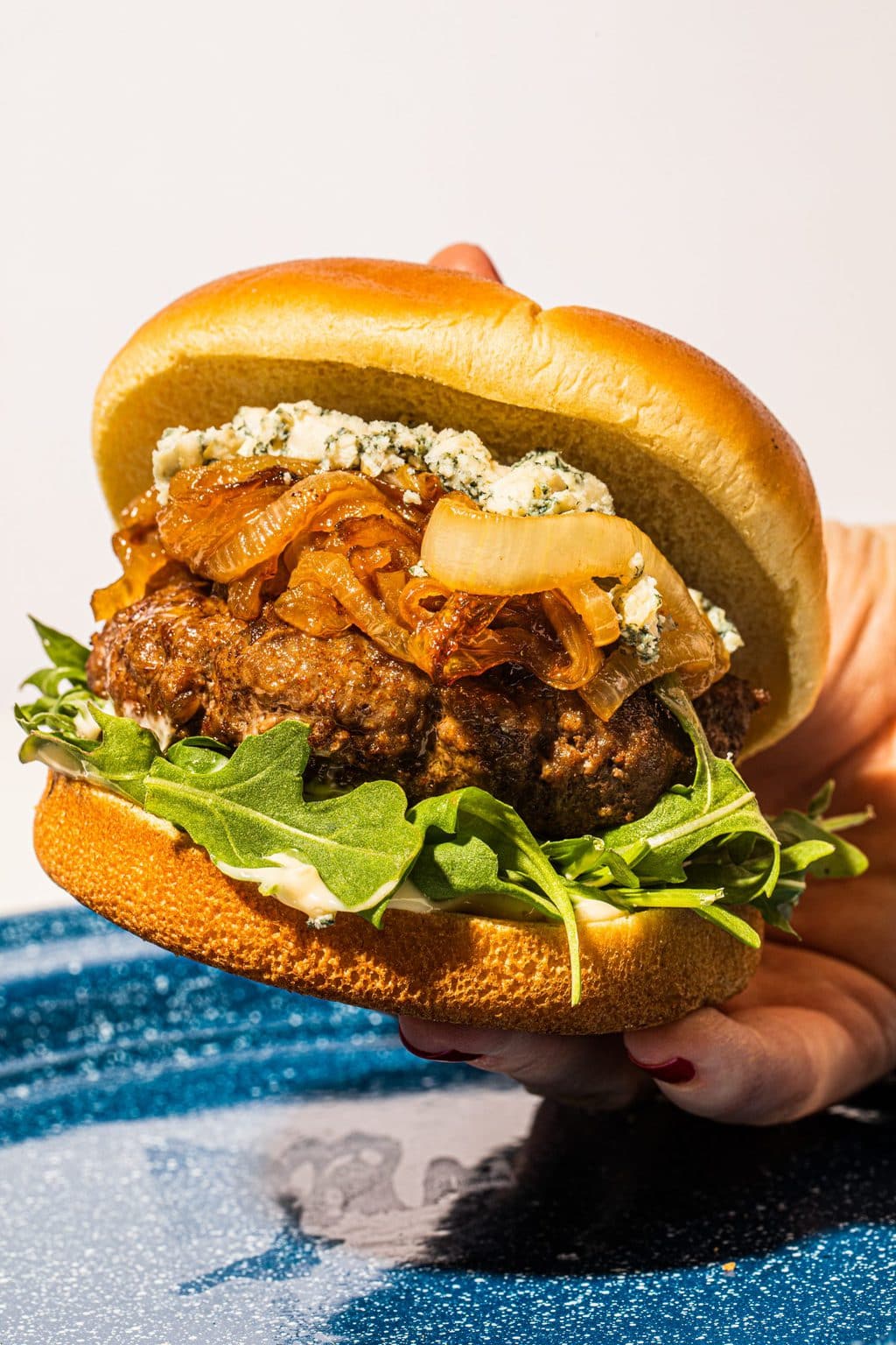 hand holding burger with blue cheese over blue plate