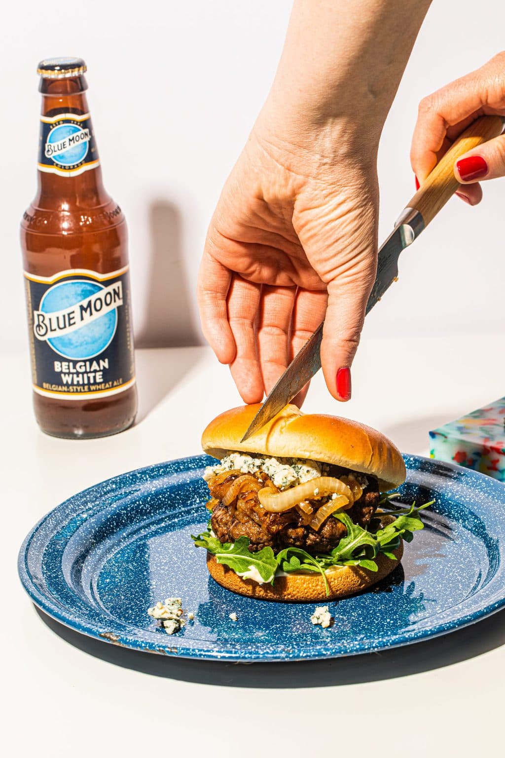 two hands cutting blue cheese burger with knife on blue plate