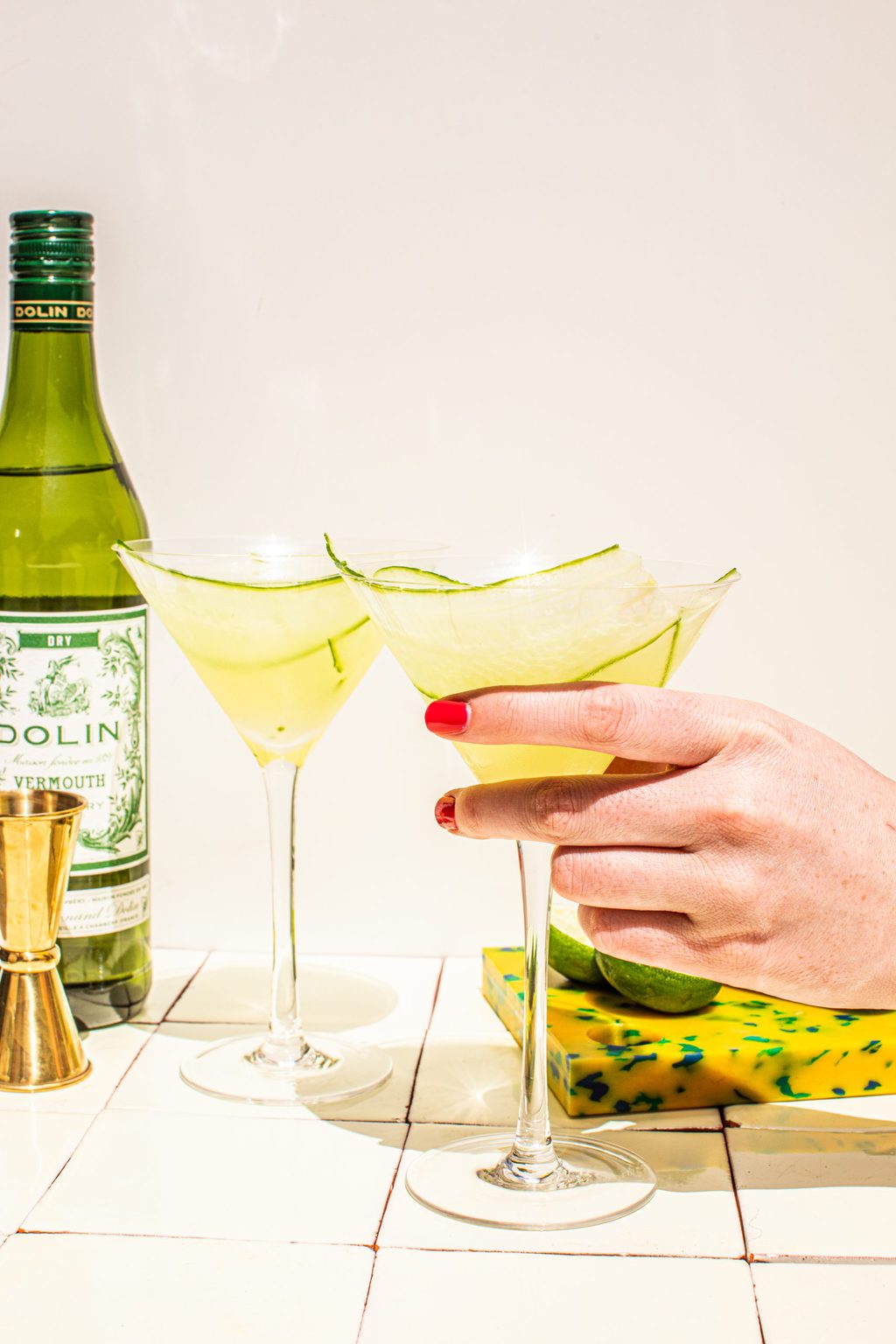 hand holding cucumber martini in glass with dry vermouth on the side