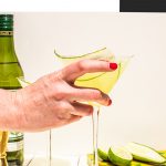 hand holding cucumber martini in glass with dry vermouth on the side