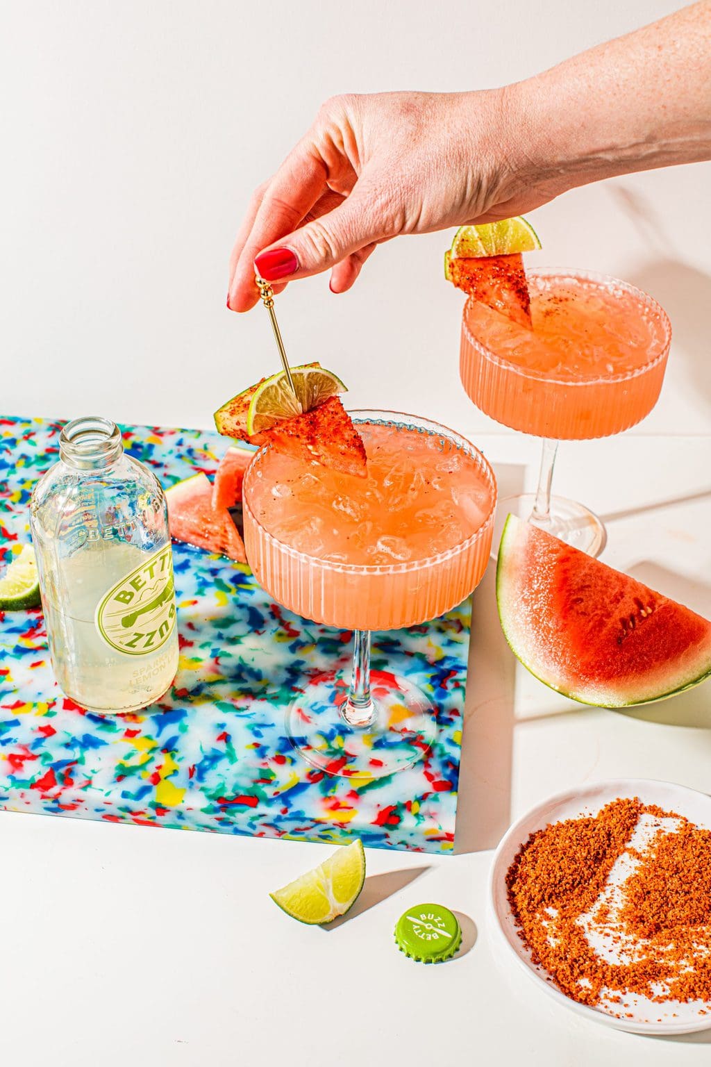 Coupe glasses filled with watermelon tequila spritzer and a hand putting the garnish on top of the glass.