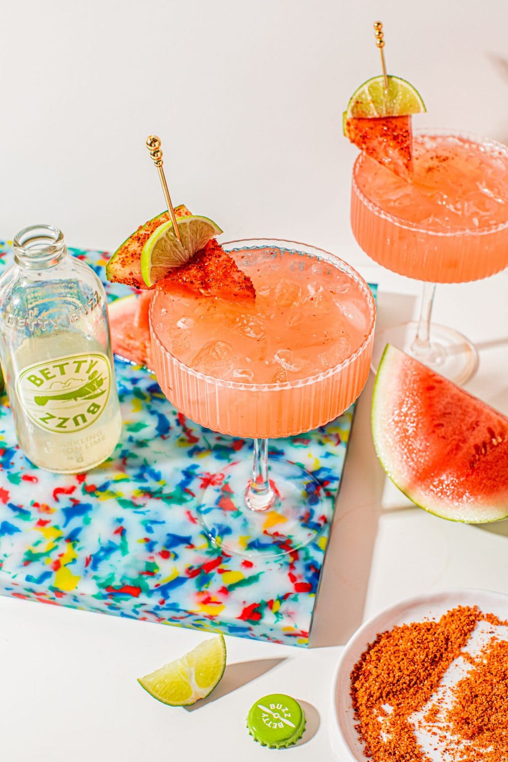 coupe glass filled with watermelon tequila spritzer topped with a watermelon wedge and lime wedge