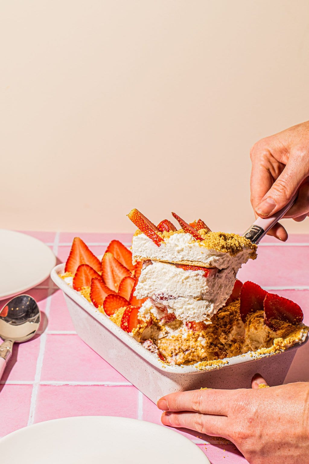 cutting large square out of strawberry ice box cake in baking dish