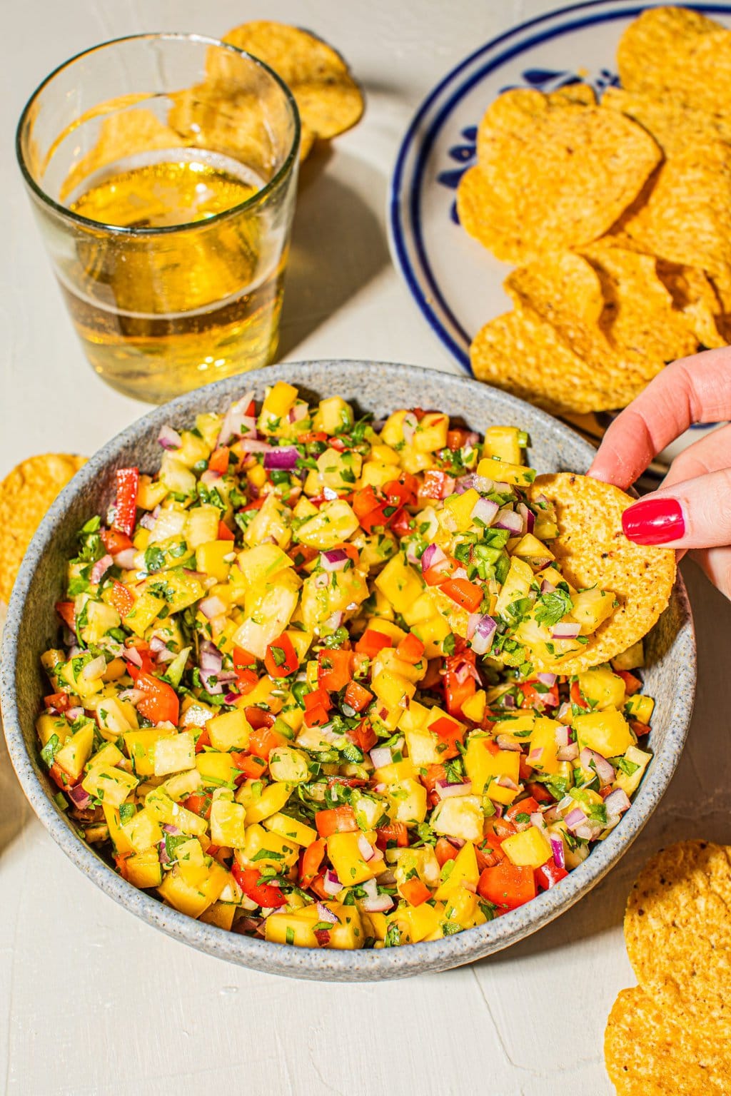 hand scooping tortilla chip into large bowl of pineapple and mango salsa