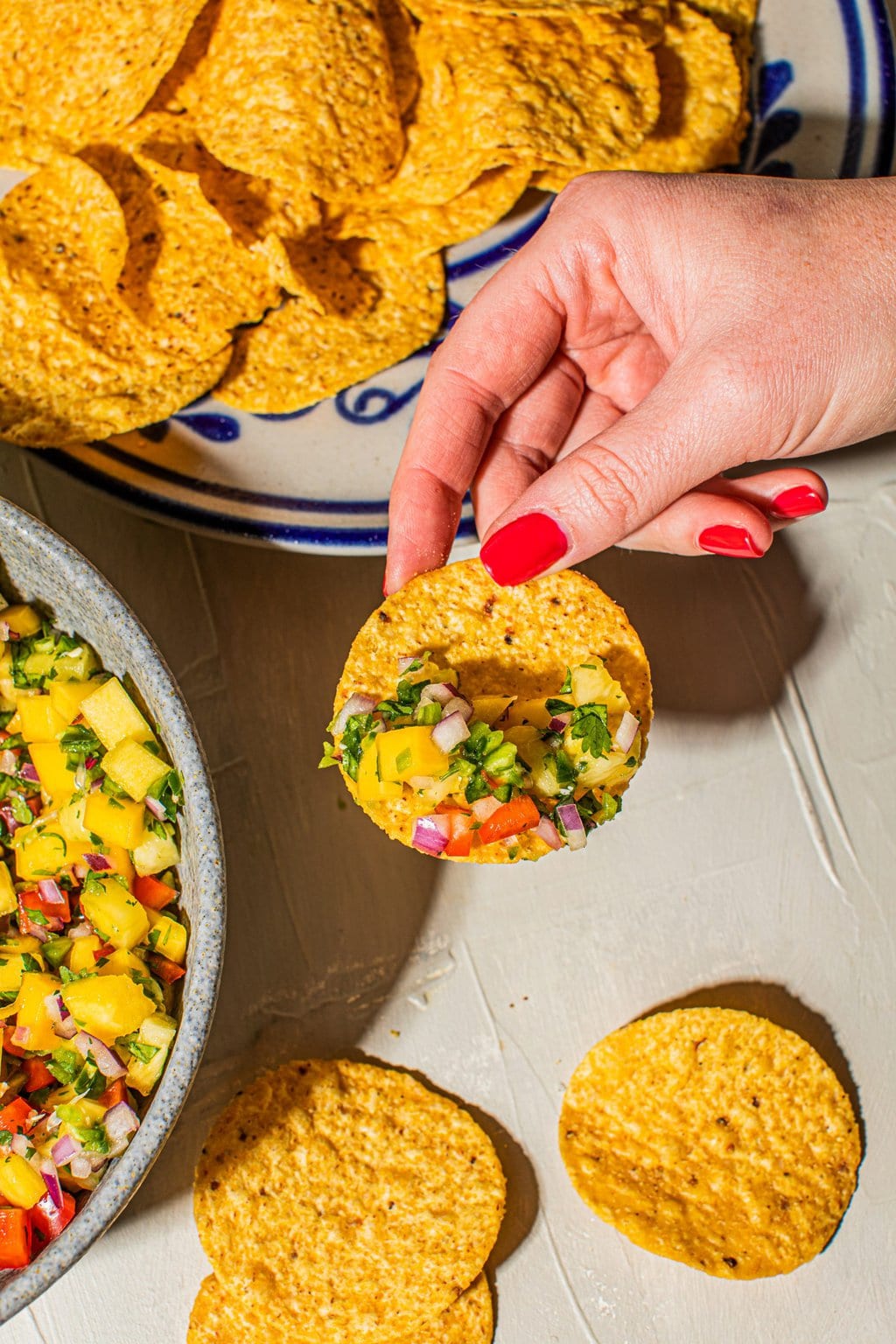 hand holding tortilla chip with scoop of pineapple mango salsa