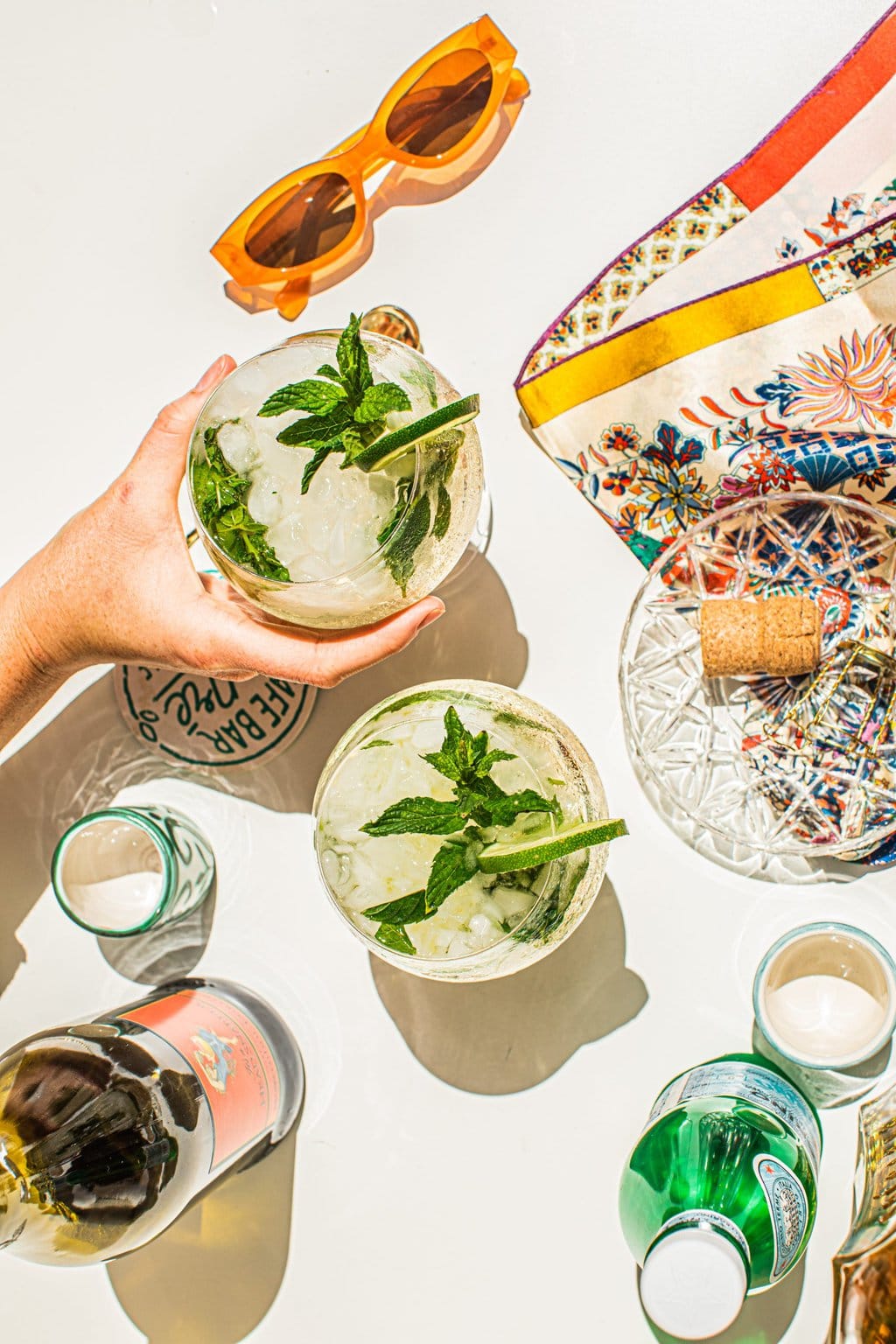 two cocktails, a pair of orange sunglasses, prosecco bottle, sparkling water bottle and an Italian silk scarf 