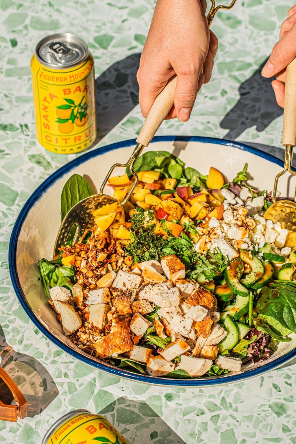 two hands tossing peach spinach salad in large bowl with tongs