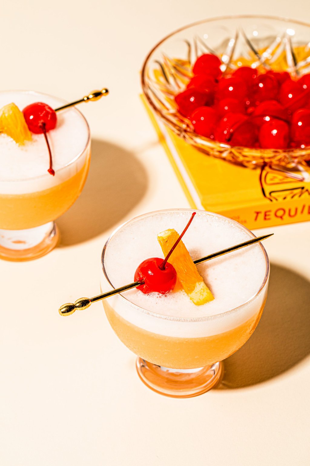 two tequila sour cocktails with bowl of maraschino cherries