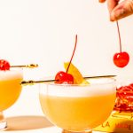 hand placing maraschino cherry on top of tequila sour recipe in glass