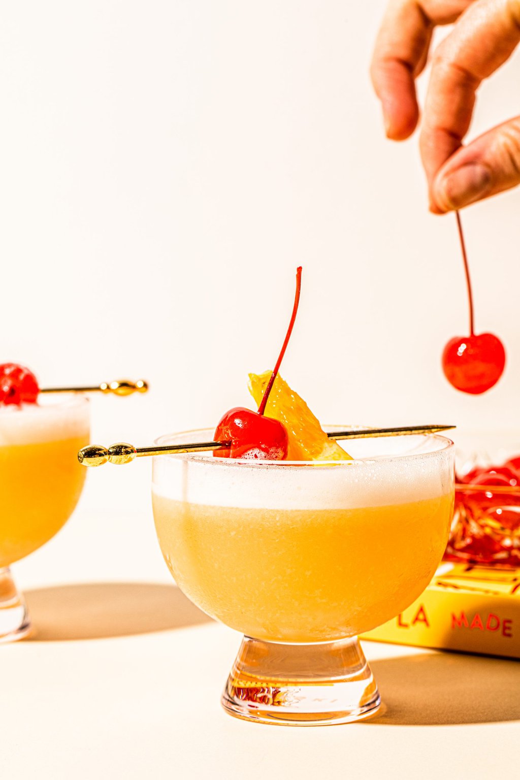 hand placing maraschino cherry on top of tequila sour recipe in glass