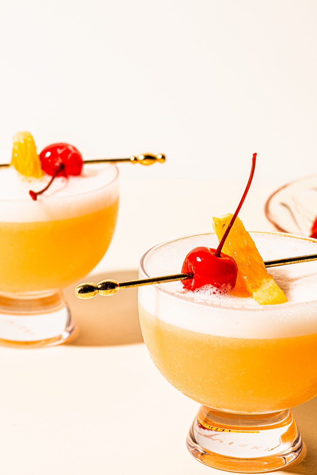 two tequila sours in glasses garnished with orange and cherry