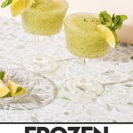 two frozen mojitos in a wine glass garnished with mint sprig and lime