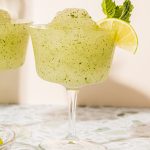 frozen mojito cocktail in a wine glass garnished with mint sprig and lime