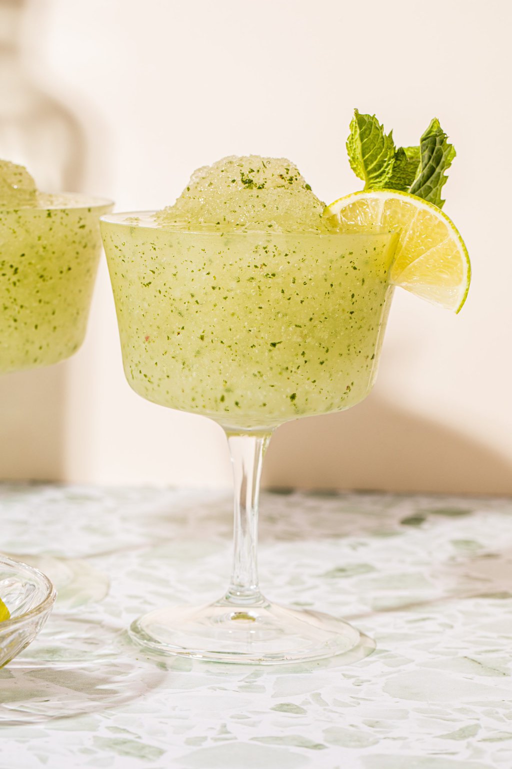 frozen mojito cocktail in a wine glass garnished with mint sprig and lime