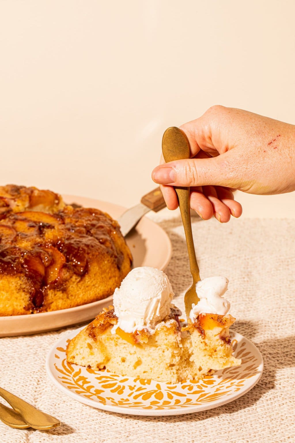 fork digging into slice of peach cake topped with vanilla ice cream