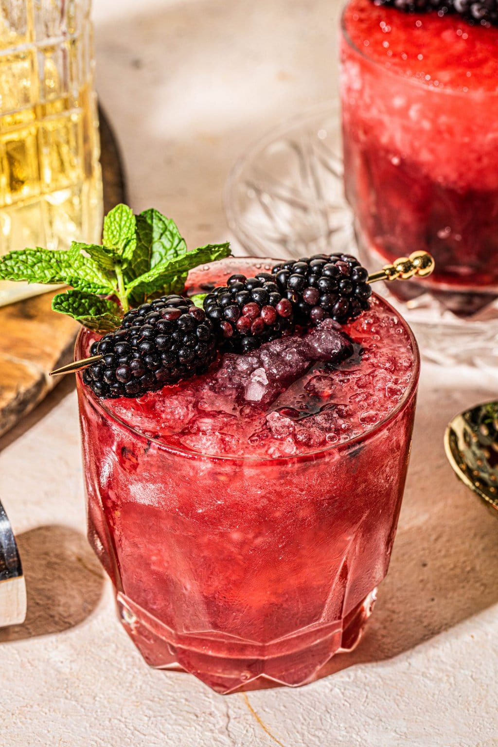 Blackberry bourbon smash in a clear glass topped with a gold cocktail pick with blackberries.