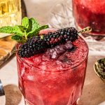 a glass filled with blackberry bourbon smash topped with a cocktail pick of blackberries