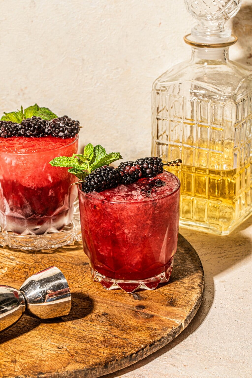 Two glasses filled with blackberry bourbon smash cocktail and a decanter filled with bourbon 