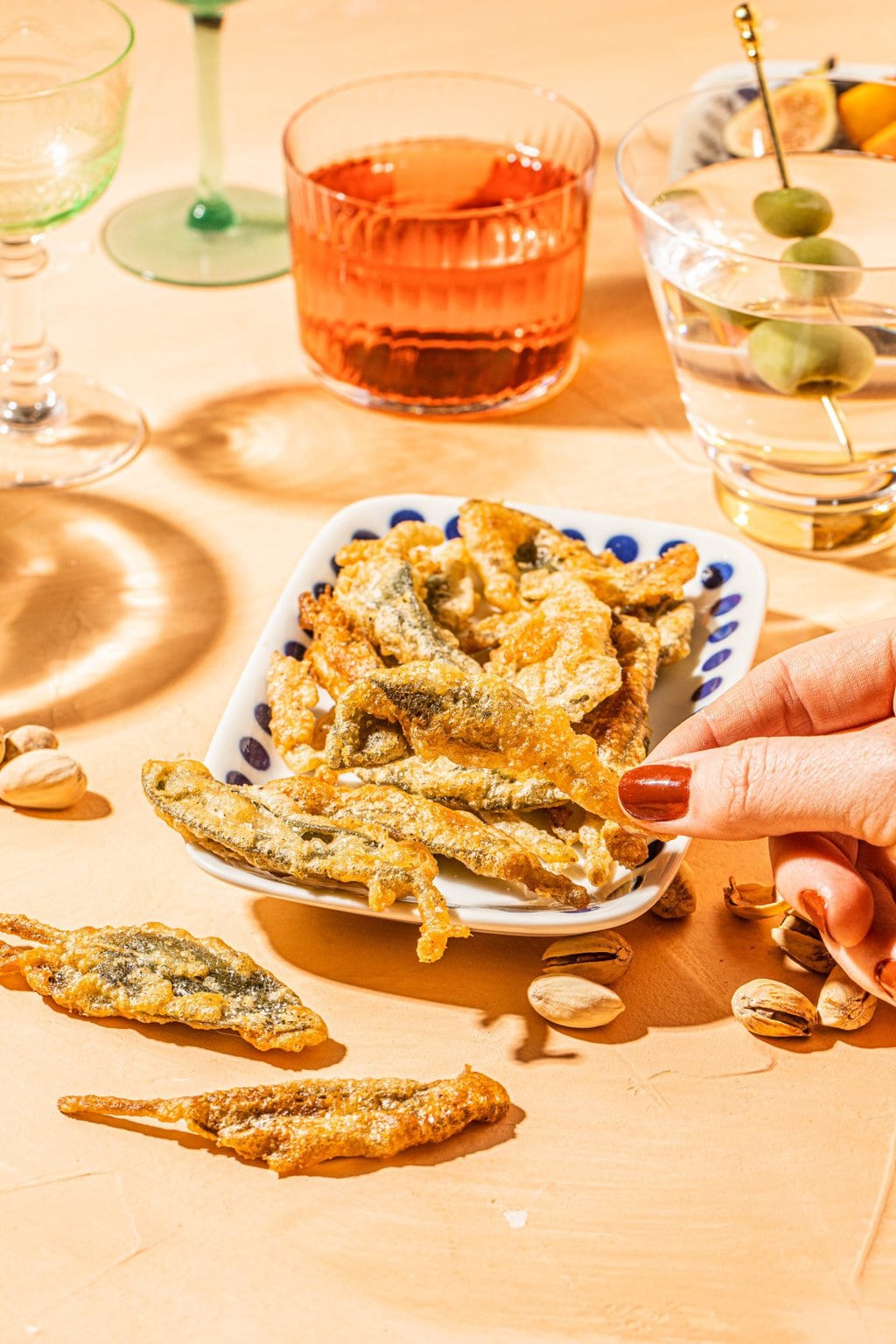 one piece of fried sage being grabbed off a white platter with blue polka dots 