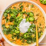 white chicken chili topped with sour cream, jalapeno slices and cilantro in white bowl with gold spoon