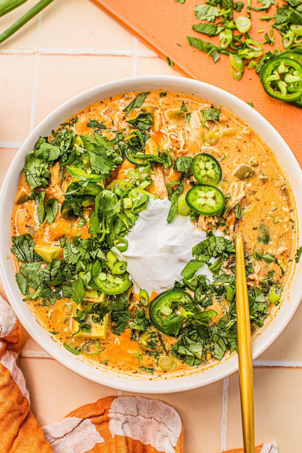 white chicken chili topped with sour cream, jalapeno slices and cilantro in white bowl with gold spoon