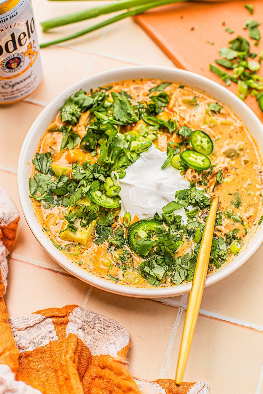 white bean chicken chili topped with sour cream, jalapeno slices and cilantro in white bowl with gold spoon