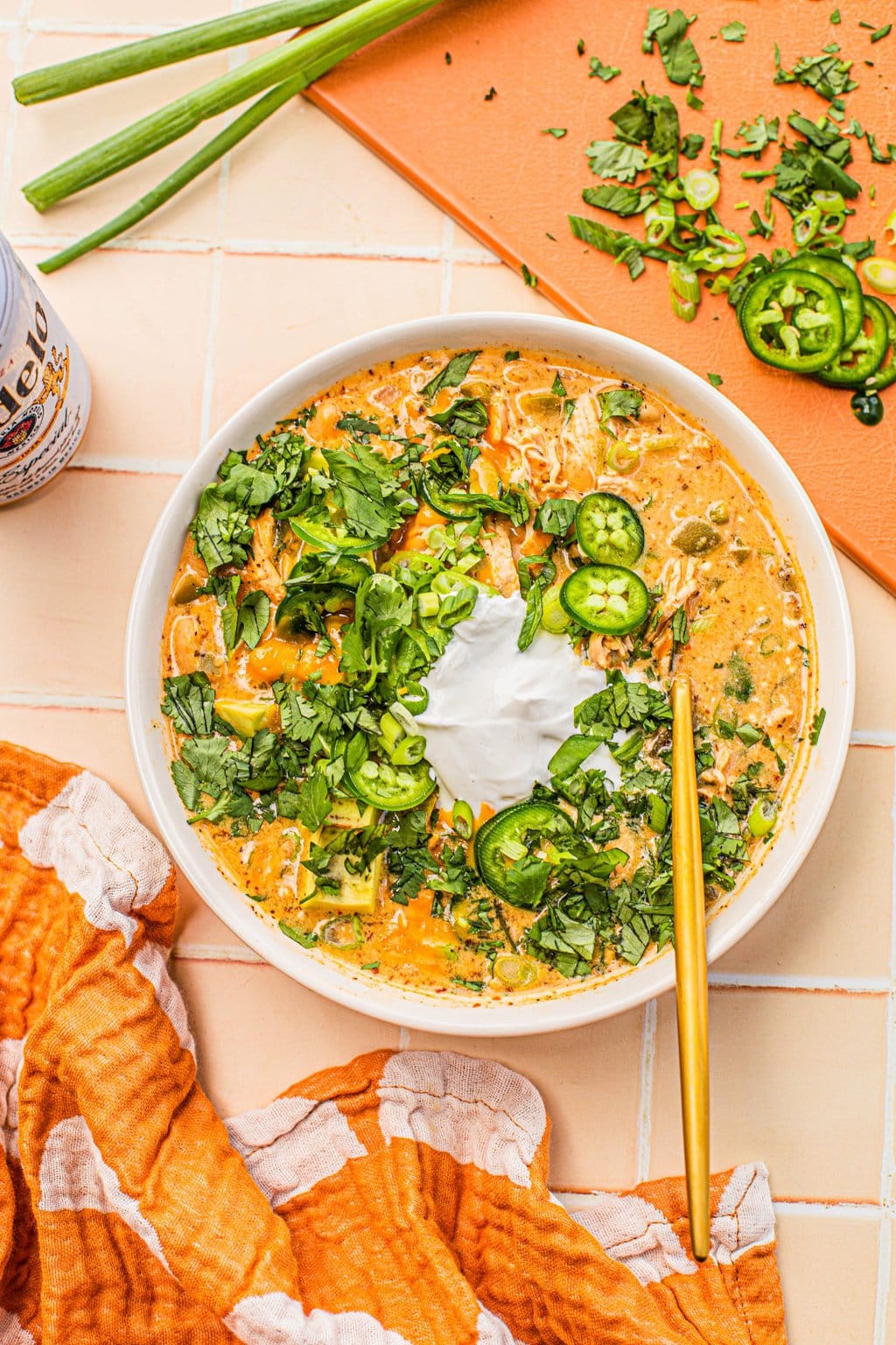 white chicken chili topped with sour cream, jalapeno slices and cilantro in white bowl with gold spoon