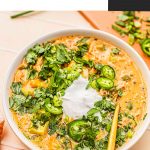 white chicken chili topped with sour cream, jalapeno slices and cilantro in white bowl with gold spoon