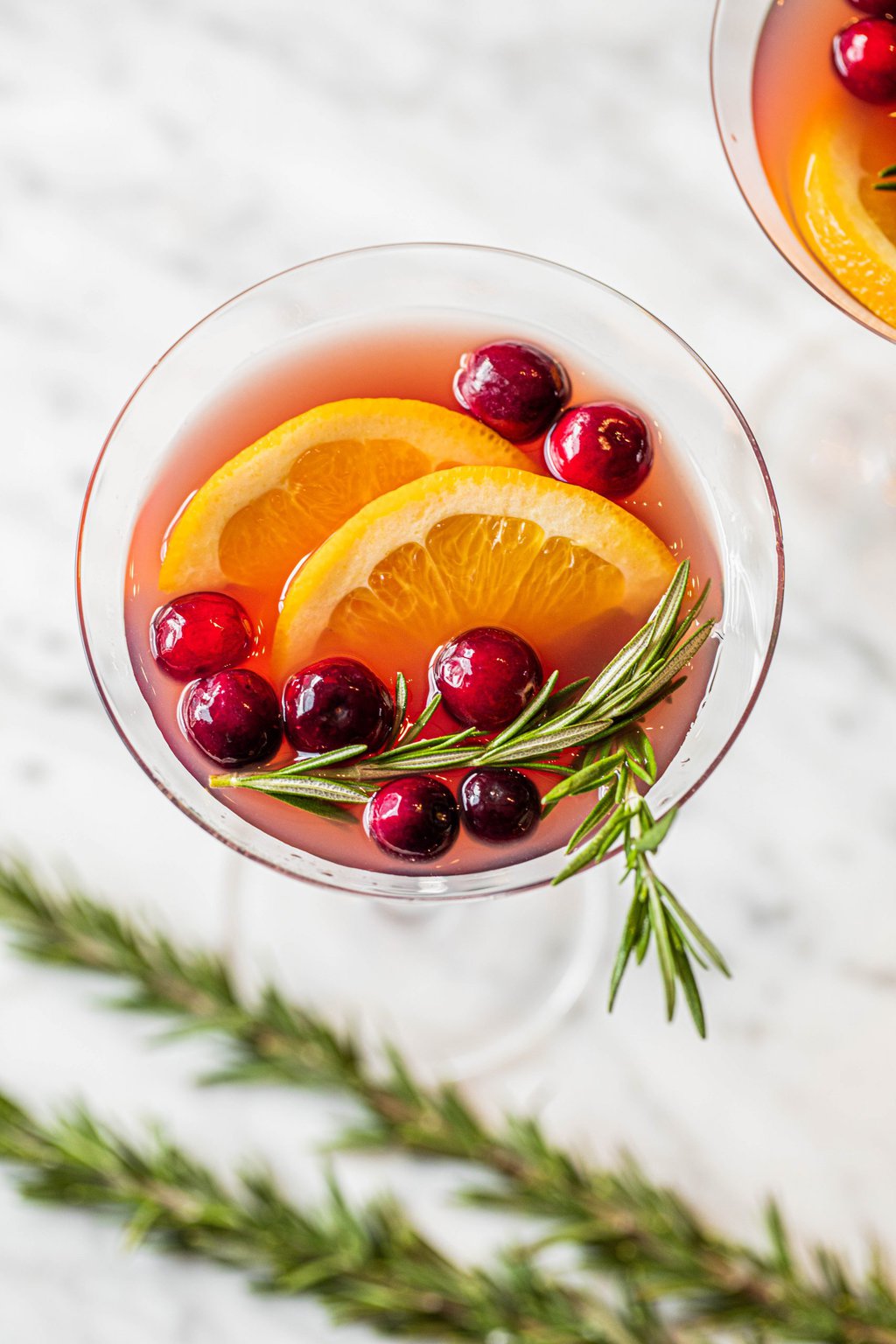 pomegranate christmas cocktail in martini glass with cranberries, orange and rosemary