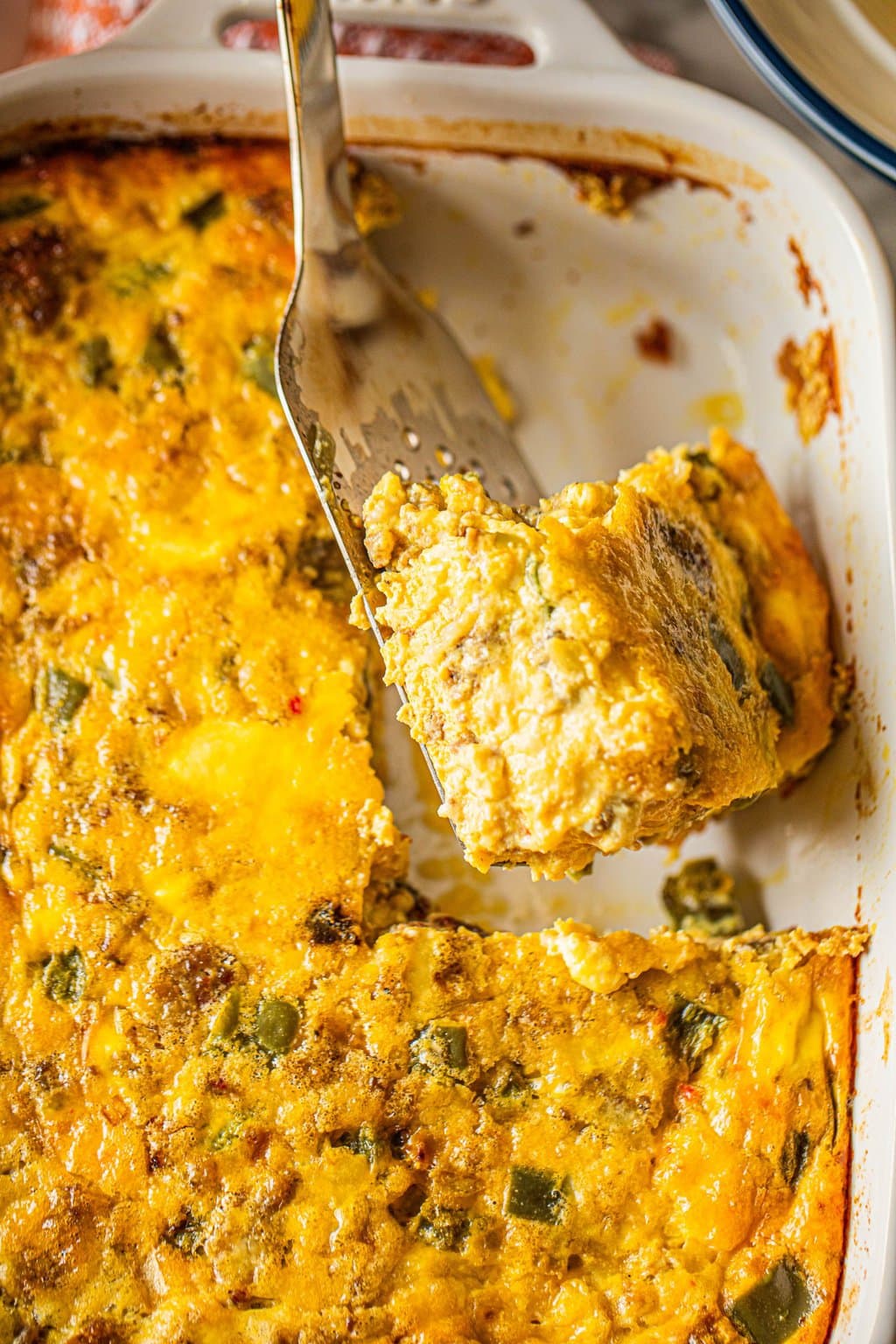 spatula lifting breakfast sausage egg casserole out of white baking dish