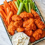 boneless buffalo chicken bites on platter with celery, carrots, blue cheese dressing