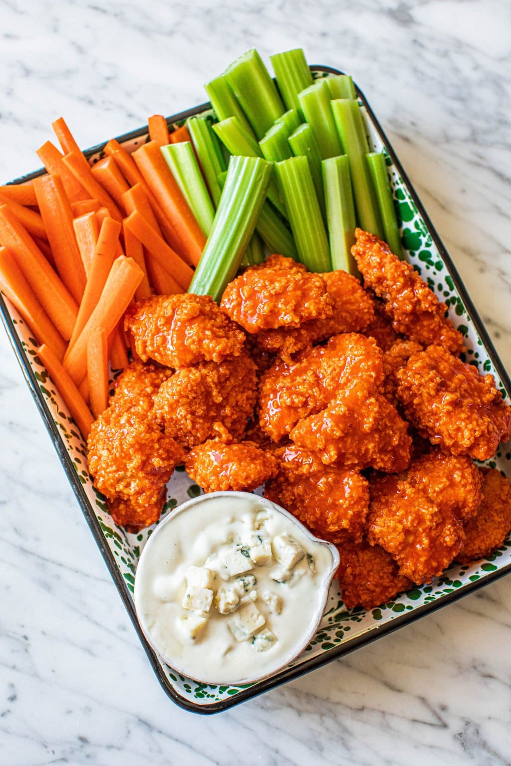 boneless buffalo chicken bites on platter with celery, carrots, blue cheese dressing