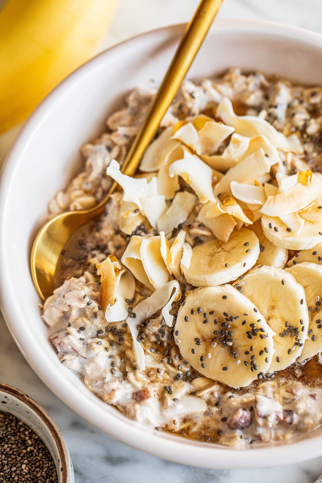 overnight oats with coconut milk in white bowl topped with banana slices and coconut flakes