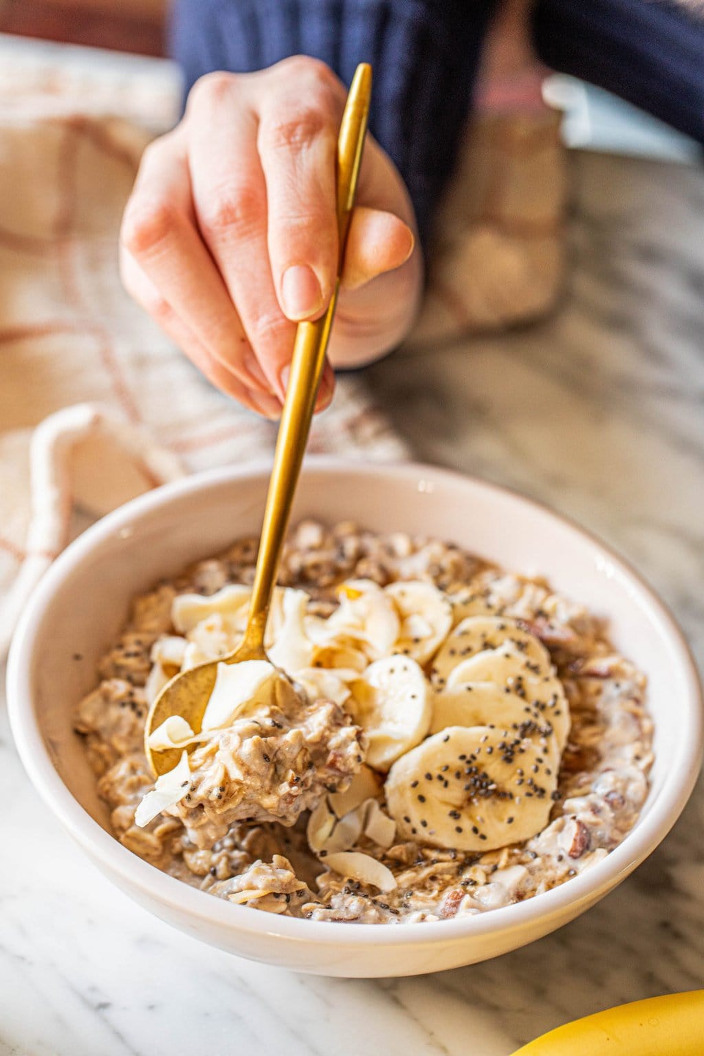 woman taking spoonful of coconut milk overnight oats in white bowl