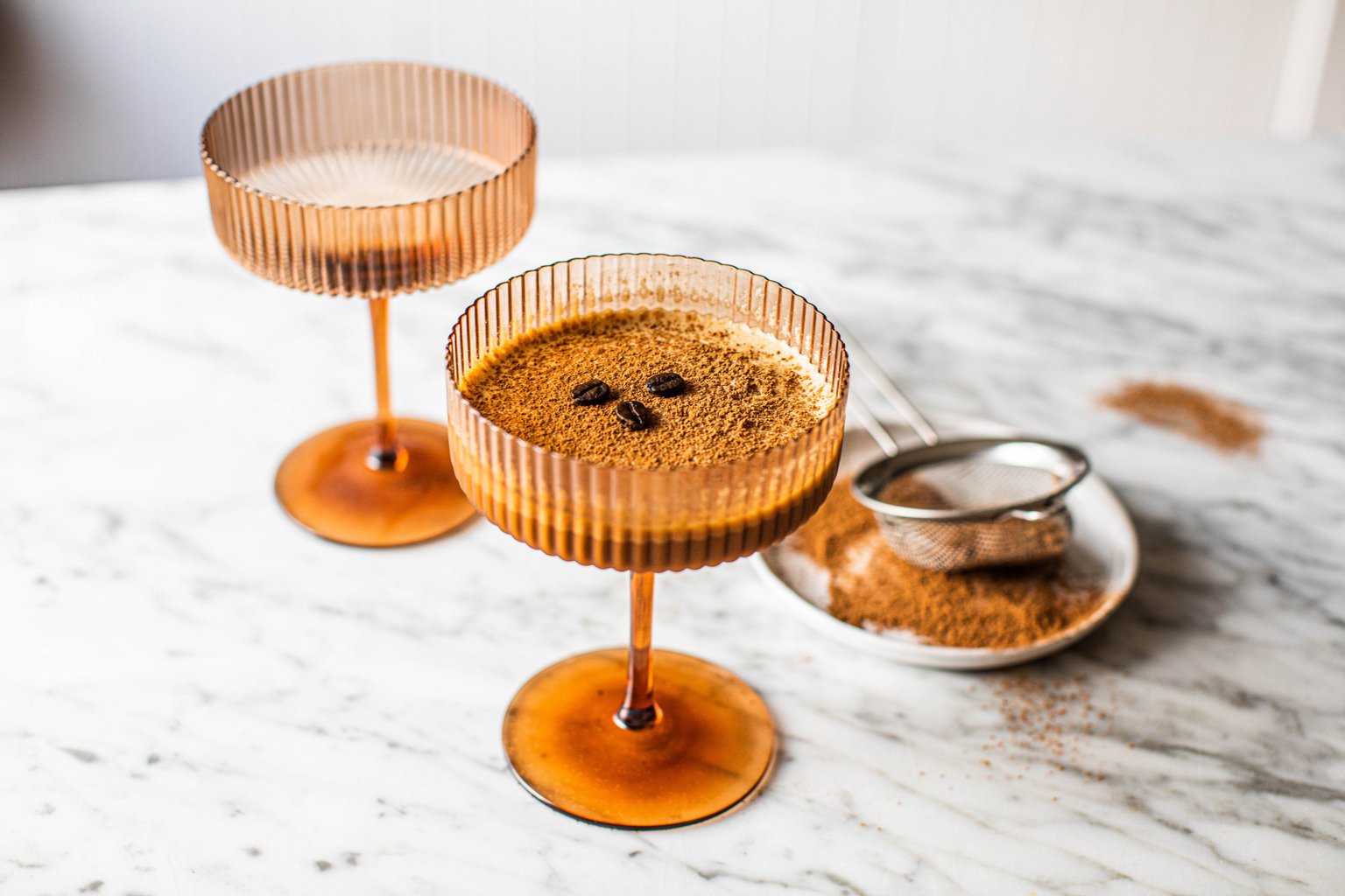 a brown coupe glass filled with non alcoholic espresso martini topped with cocoa powder and espresso beans