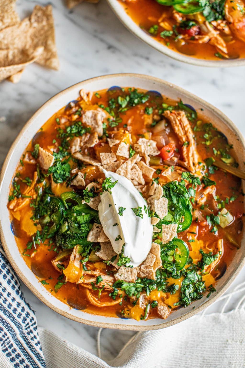 A bowl of healthy chicken tortilla soup topped with sour cream, jalapeños, cilantro, and tortilla chips 