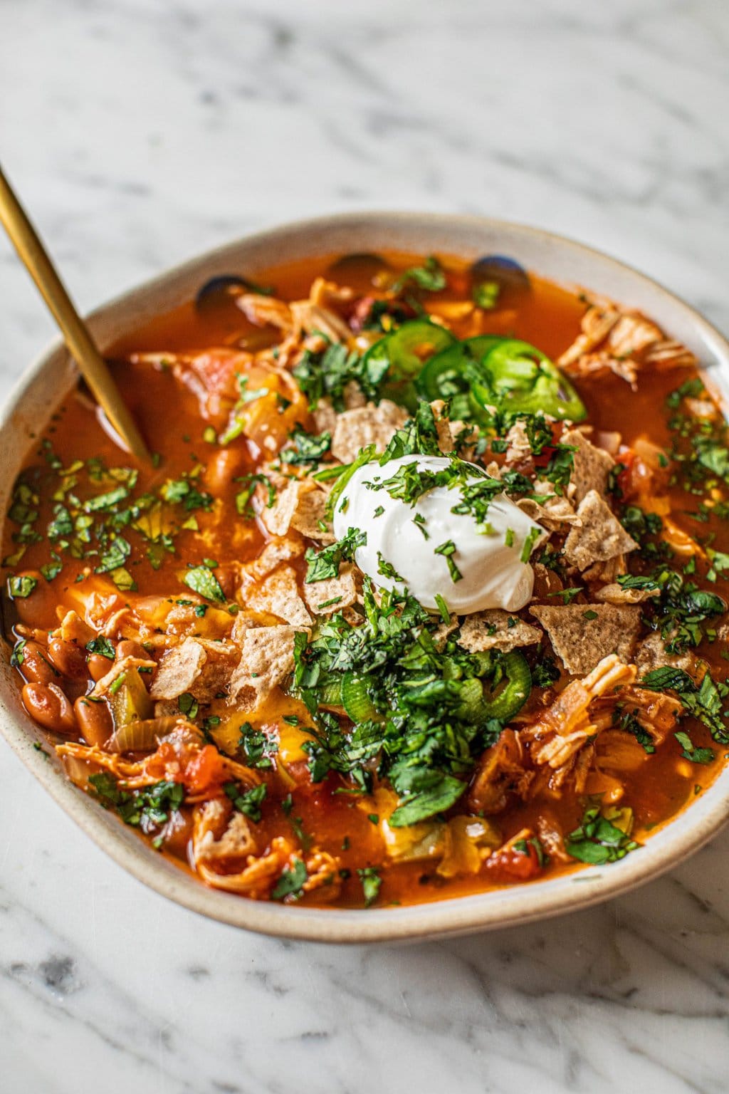 A bowl of healthy chicken tortilla soup topped with sour cream, cilantro, jalapeños, and crumbled tortilla chips. 