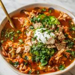 A bowl of healthy chicken tortilla soup topped with sour cream, chopped cilantro, jalapeños, and crumbled tortilla chips