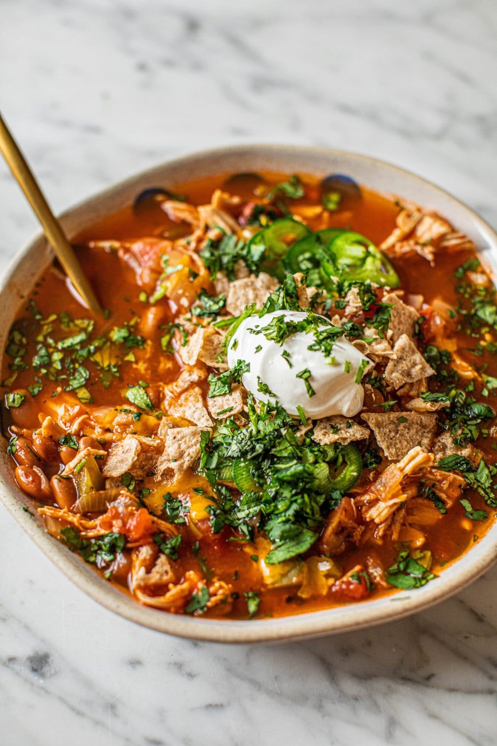 A bowl of healthy chicken tortilla soup topped with sour cream, chopped cilantro, jalapeños, and crumbled tortilla chips