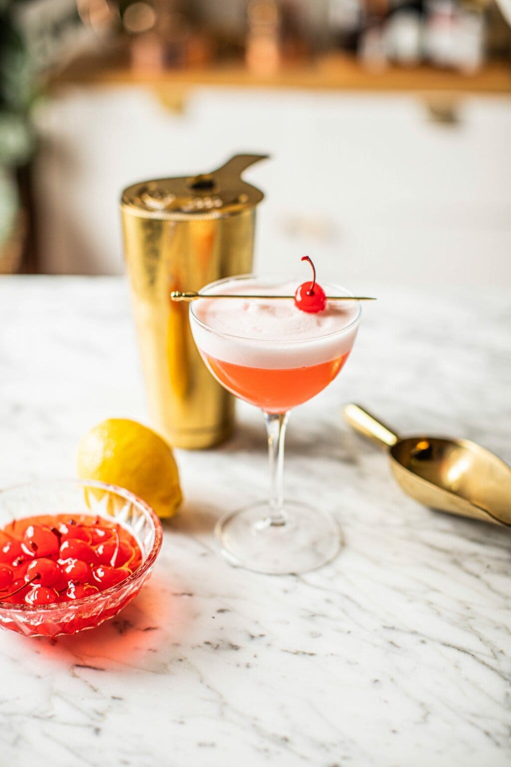 pink cocktail in coupe glass with gold cocktail shaker and ice scoop