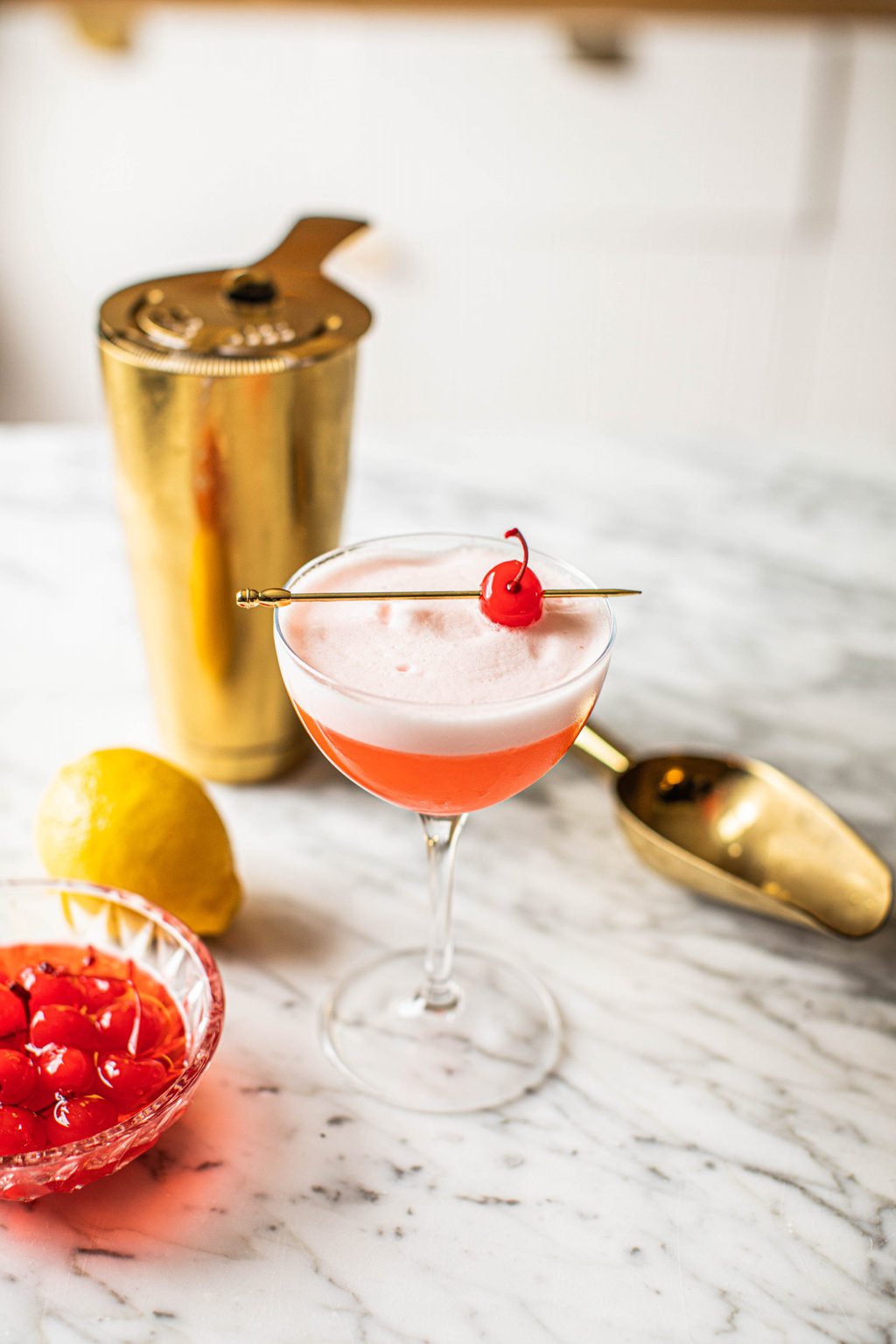 pink cocktail in coupe glass with gold cocktail shaker and ice scoop