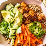 salmon quinoa bowl topped with cucumber, carrots, avocado, jalapenos