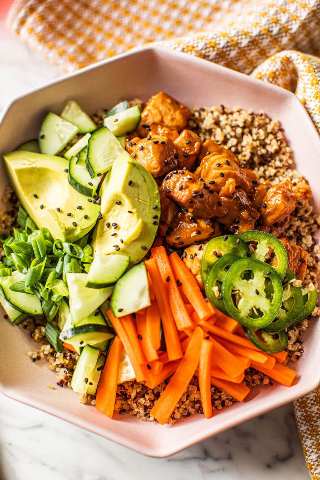 salmon quinoa bowl topped with cucumber, carrots, avocado, jalapenos