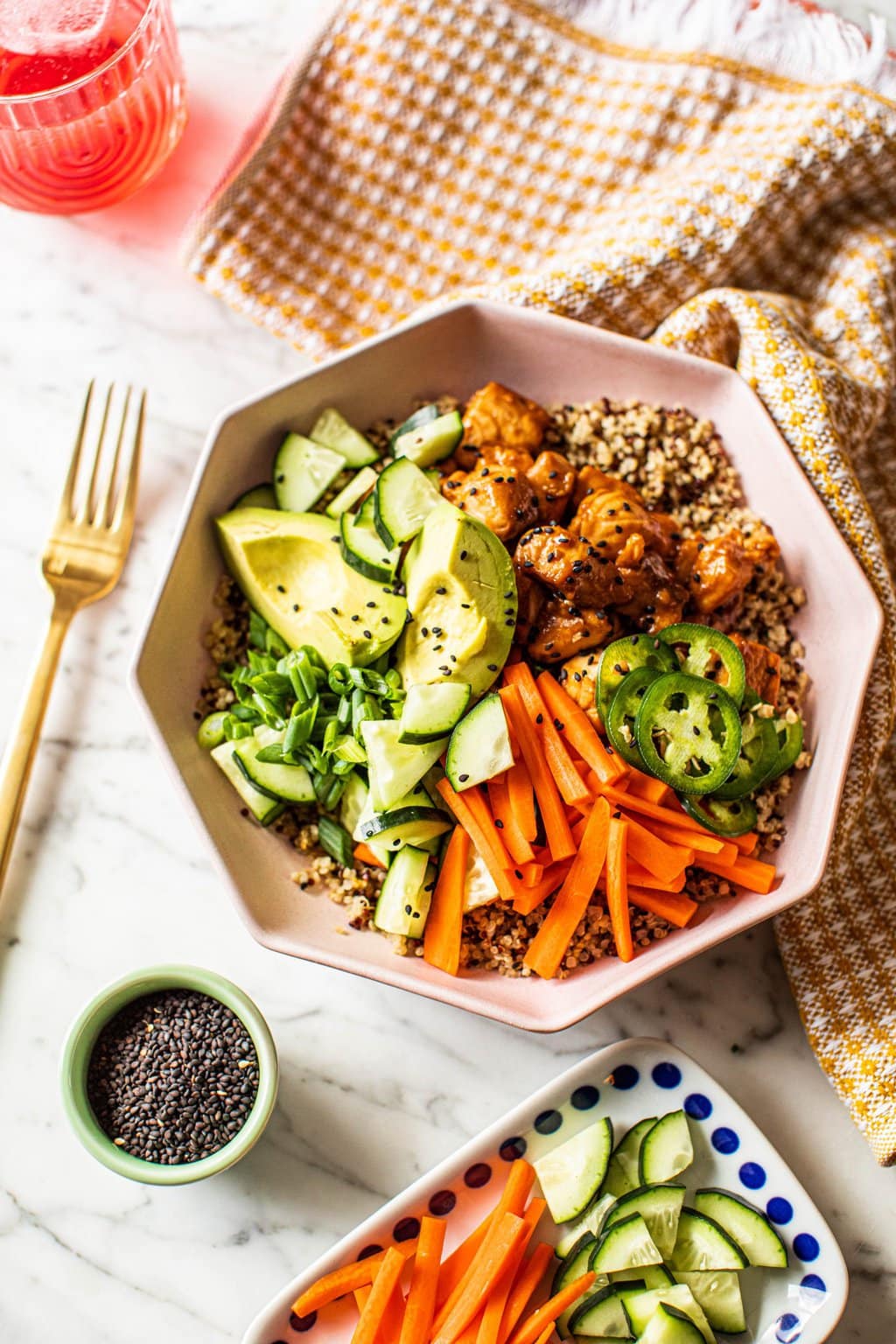 salmon quinoa bowl recipe topped with cucumber, carrots, avocado, jalapenos