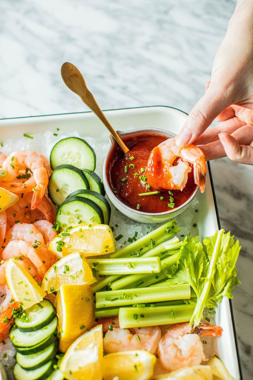 hand dipping shrimp into cocktail sauce on platter